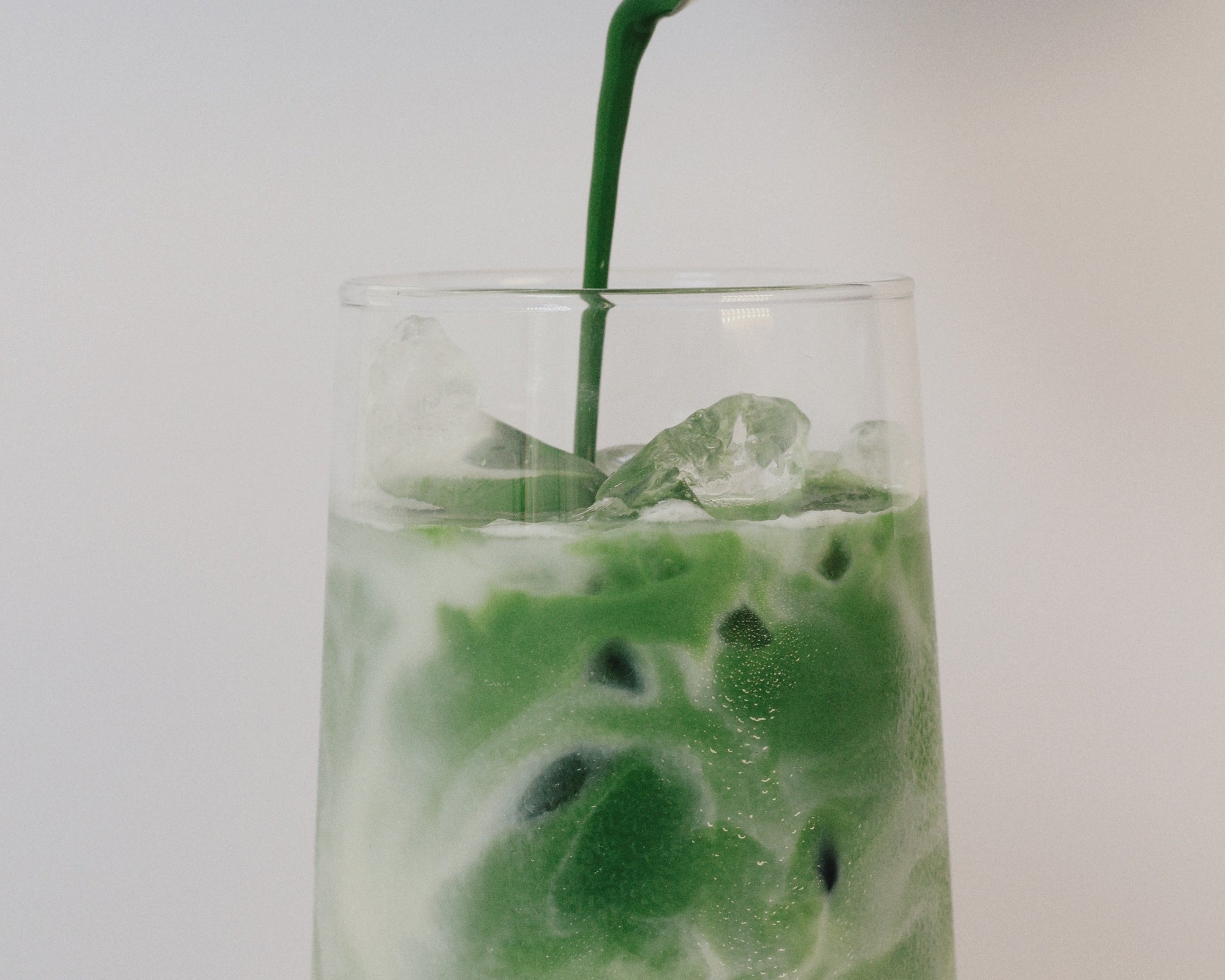 Matcha being poured into a glass with ice on a white background
