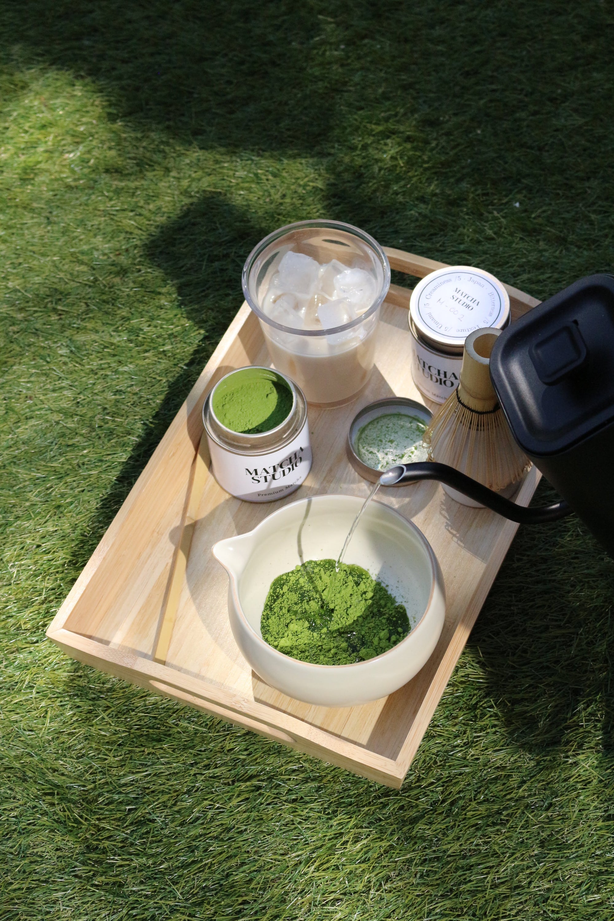 Tea-making setup with a wooden tray, teapot, and containers on grass