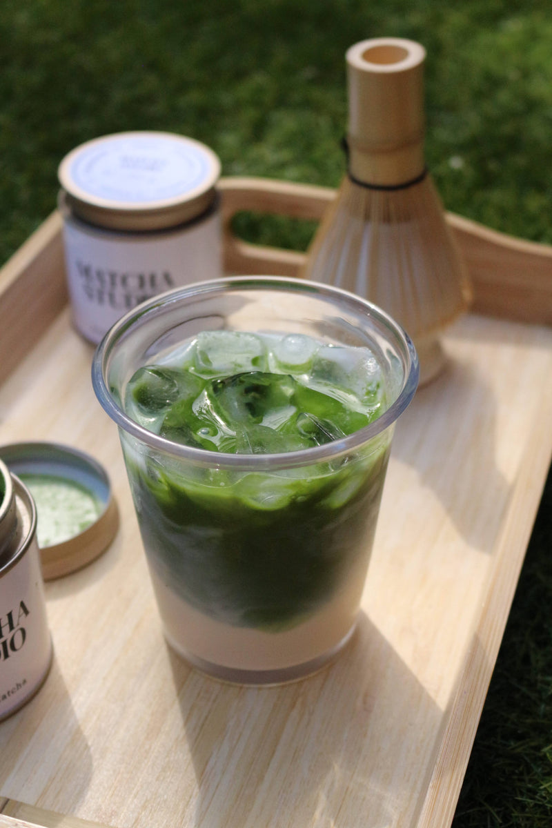matcha iced drink in a clear cup on a wooden tray outdoors