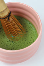 Closeup on whisked matcha in pink bowl, with a bamboo whisk inside.