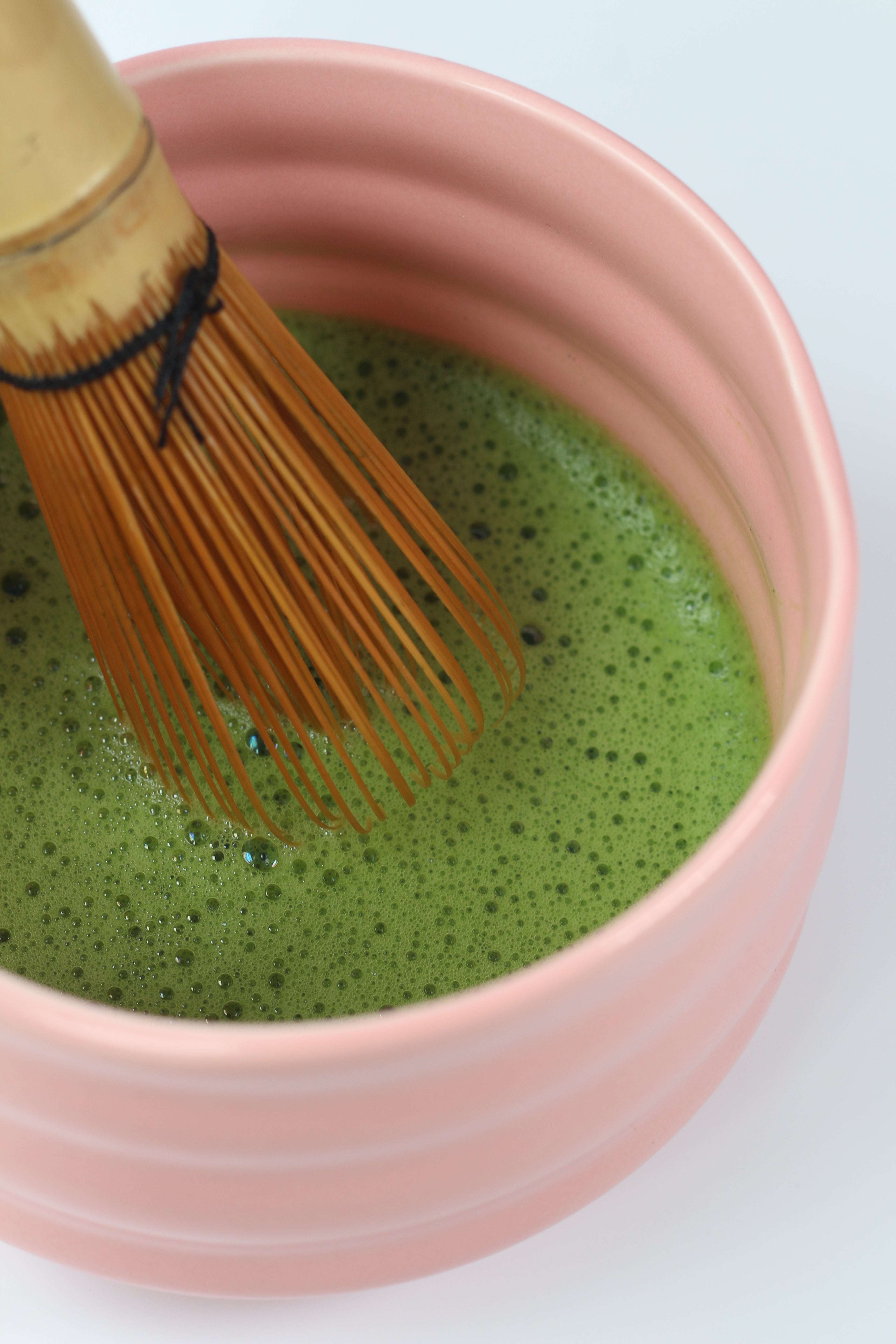 Closeup on whisked matcha in pink bowl, with a bamboo whisk inside.